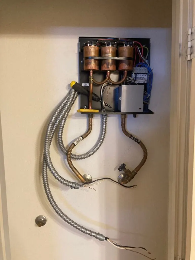 An electric tankless water heater mounted in a closet, with its supply lines and wiring connected.