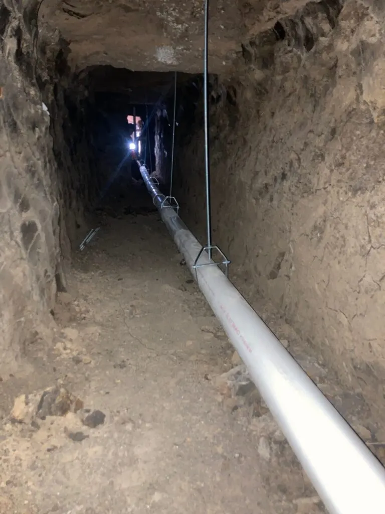 A long run of new PVC drain pipe hung level through a tunnel under a home.