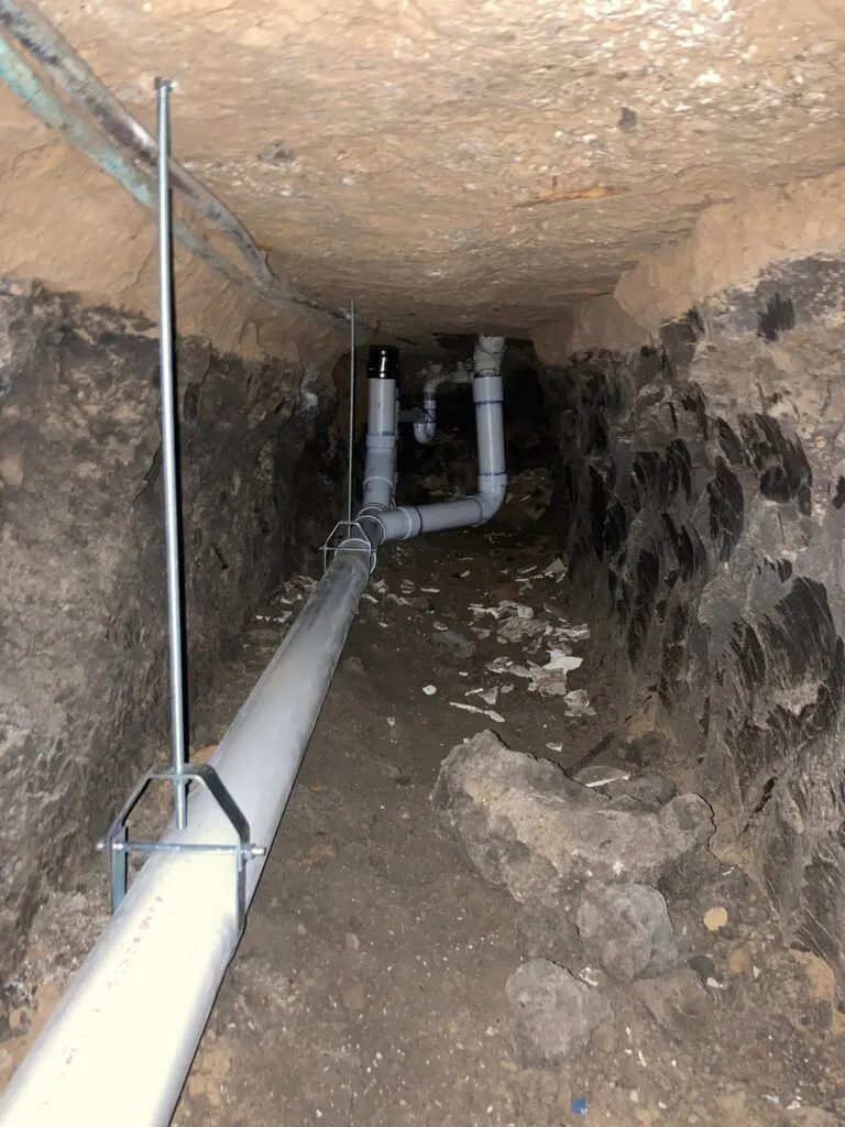 New PVC drain risers under a slab, tied into the main line in a hand-dug tunnel.